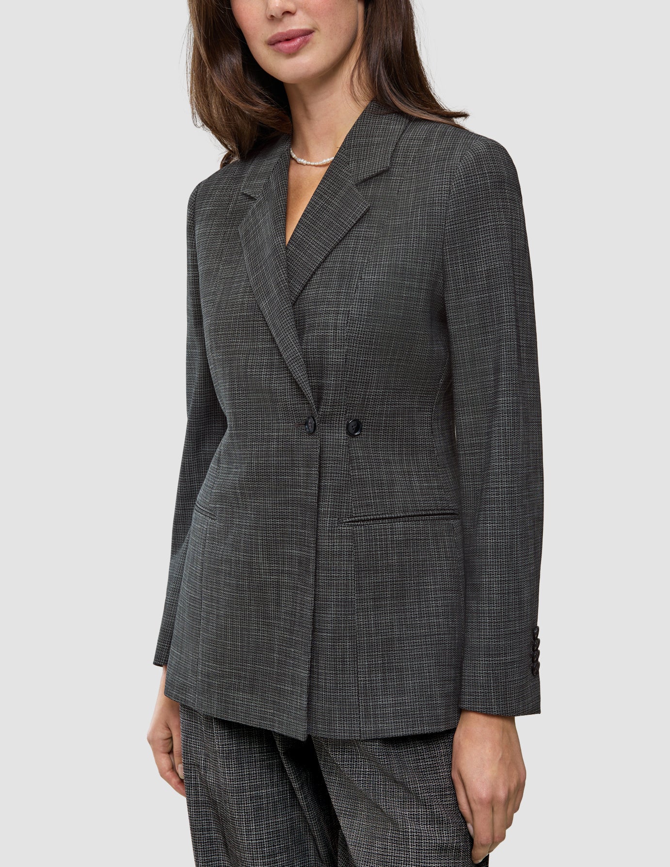 A woman wearing the Women Nara Blazer Fitted Black Check, a tailored, double-breasted blazer in a black and white checkered Scandinavian design.